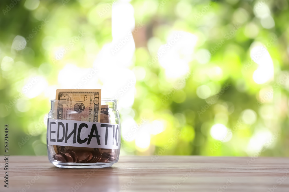 Glass jar with money and word EDUCATION on table against blurred background, space for text