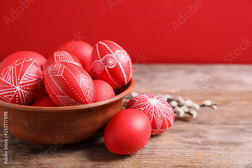 Canvas Print Wooden bowl with red painted Easter eggs on table against color background, spac