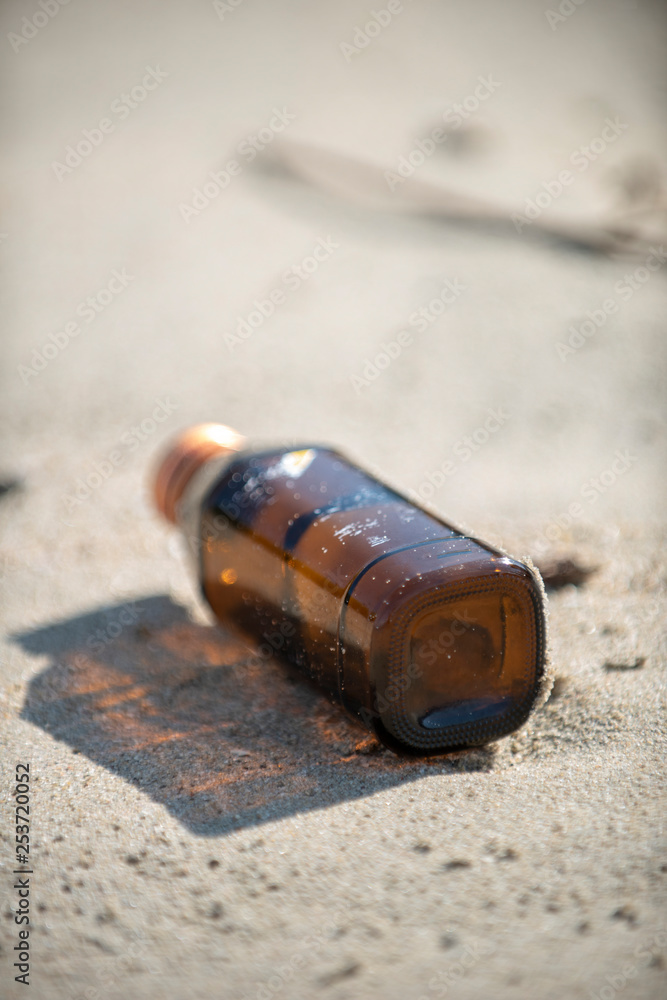 An empty brown clear bottle with cap left on the beach. A starting point of the environment problem. An empty brown clear bottle with cap left on the beach. A starting point of the environment problem.