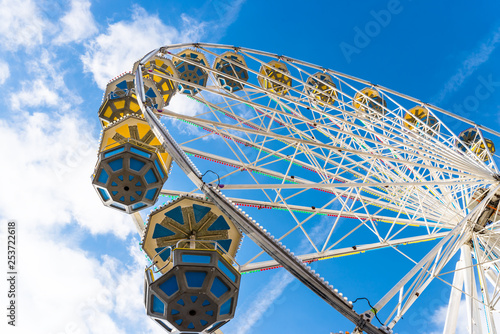 Ferris wheel with colorful gondolas in a funfair, against a beautiful blue sky with white clouds.