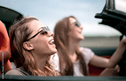 two fashionable girls travel in a convertible car.