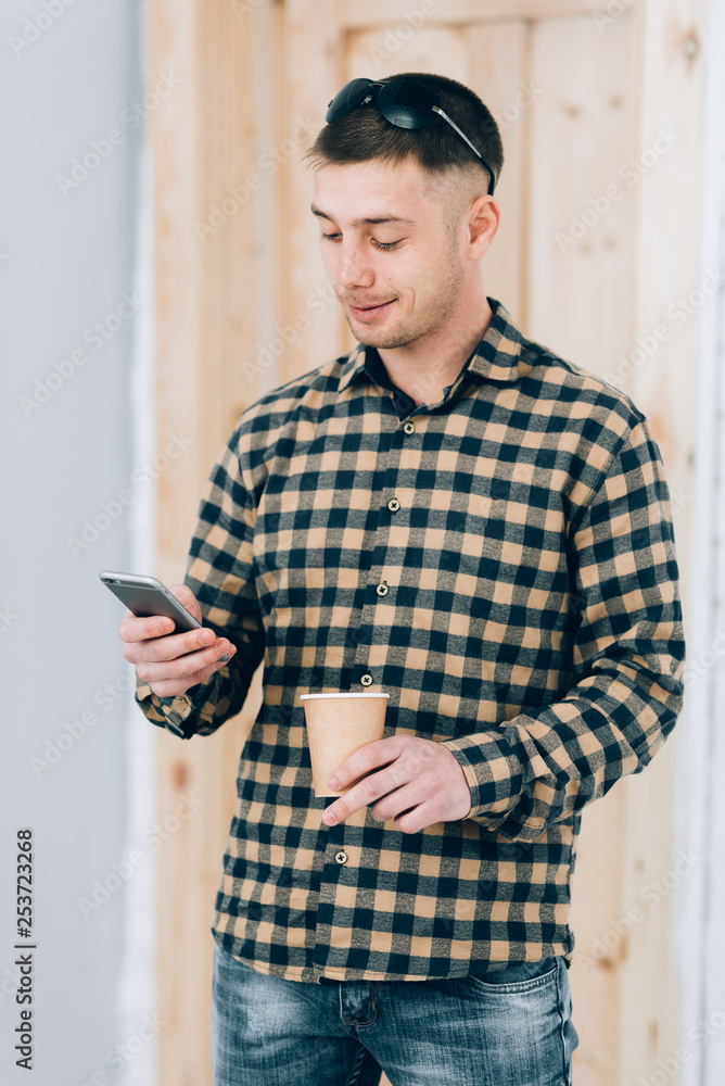 A handsome man in a plaid shirt on a brick background drinks coffee from a paper Cup A handsome man in a plaid shirt on a brick background drinks coffee from a paper Cup