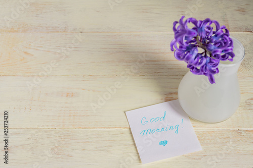 Good morning paper tag and purple hyacinth flower in white vase on wooden table