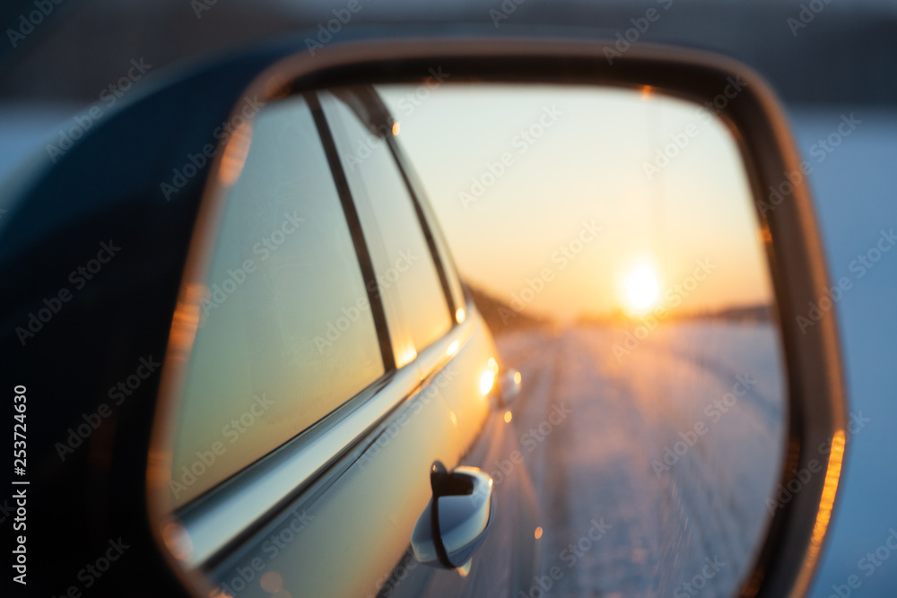 The winter road is reflected in the car's rear-view mirror. Sunset in winter.
