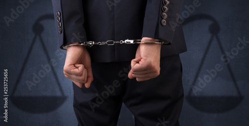 Arrested businessman in handcuffs with hands behind back and justice symbol wallpaper 