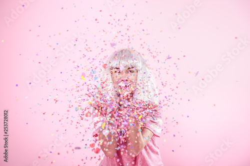 Funny Girl with silver hair gives a smile and emotion on pink background. Young woman or teen girl with confetti photo