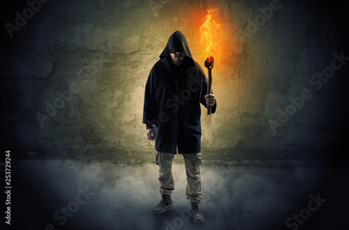 Ugly wayfarer with burning torch in his hand in front of a crumbly wall concept 