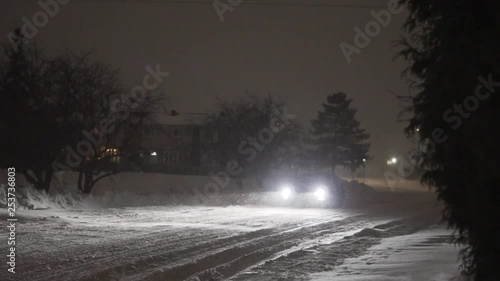 The snow coming across a roadway with a signle car coming towards the camera. photo