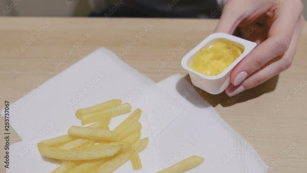 Woman is eating French fries with cheese sauce in cafe. Close-up hands. Woman is eating French fries with cheese sauce in cafe. Close-up hands.