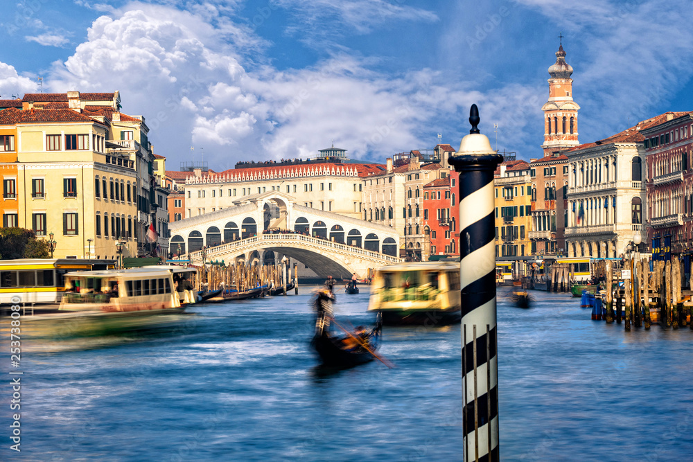 Traditional Gondola on famous Canal Grande with Rialto Bridge in background during beautiful summer day in Venice, Italy.