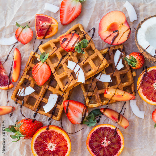Waffles with strawberries, coconut, plum and orange with chocolate