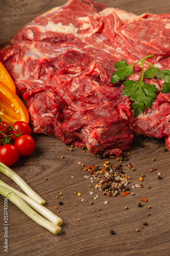 Raw beef on a wooden background with spices and vegetables.