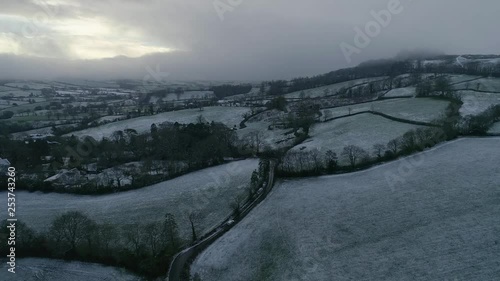 Monotone looking drone shot of a wintry snowy scene in east Devon farmland following a country road and a car driving in icy conditions. Fog cloud on the horizon photo