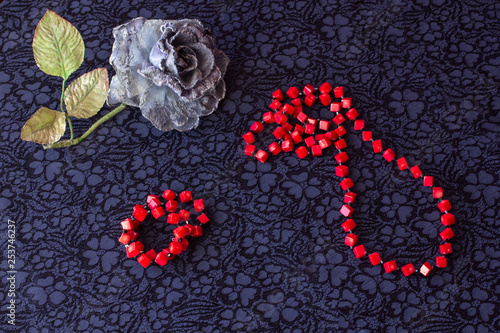 still life of artificial rose with red beads and bracelet on textile background. photo