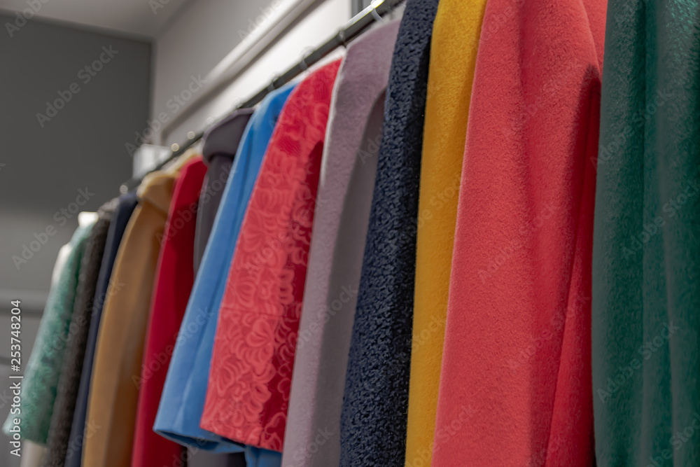Multicolored clothes hanging on hangers in a row. Coats of different styles are stored in the dressing room or shop window. Background color composition with a blurred perspective.