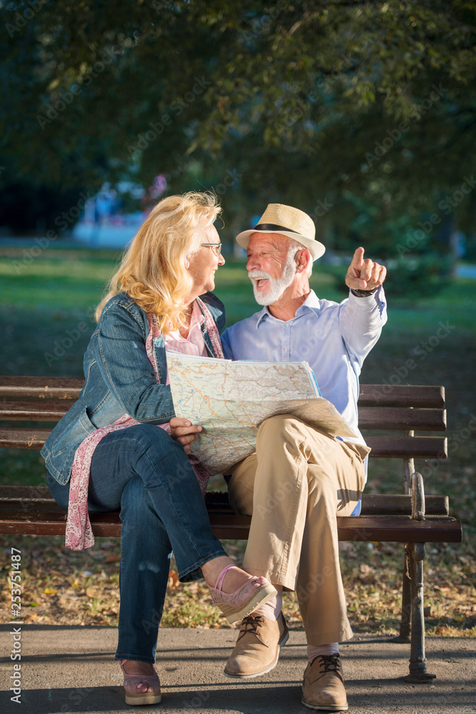 Portrait of happy man and woman reading map while sitting on a park bench. Senior couple on vacation using city map. Portrait of happy man and woman reading map while sitting on a park bench. Senior couple on vacation using city map.