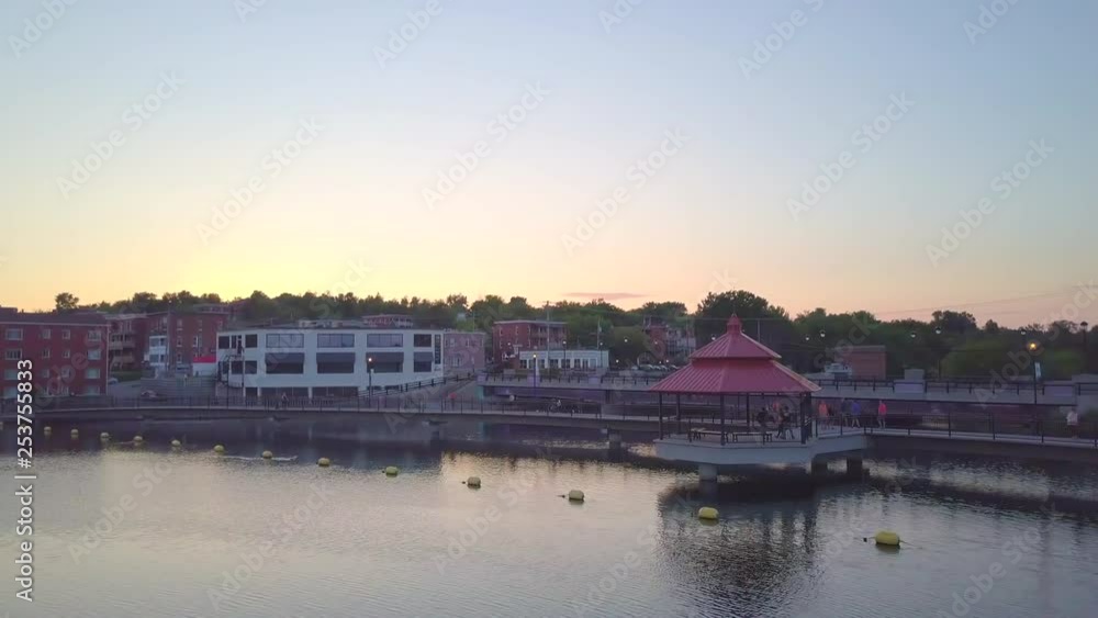 Drone moving sideways near downtown on a small city during sunset, over the lake, with buildings, cars passing by and pedrestians wandering - summer season beautiful landscape. Drone moving sideways near downtown on a small city during sunset, over the lake, with buildings, cars passing by and pedrestians wandering - summer season beautiful landscape.