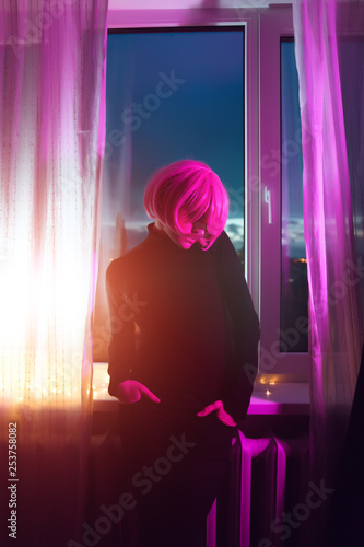 Fashion woman pink hair near the window. Pink light. Life style. Retro wave neon noir lights color toningt