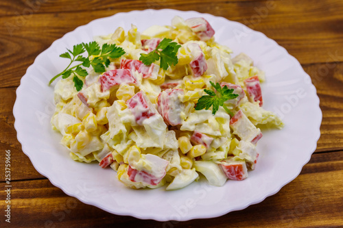 Salad with crab sticks, sweet corn, chinese cabbage, eggs and mayonnaise on wooden table