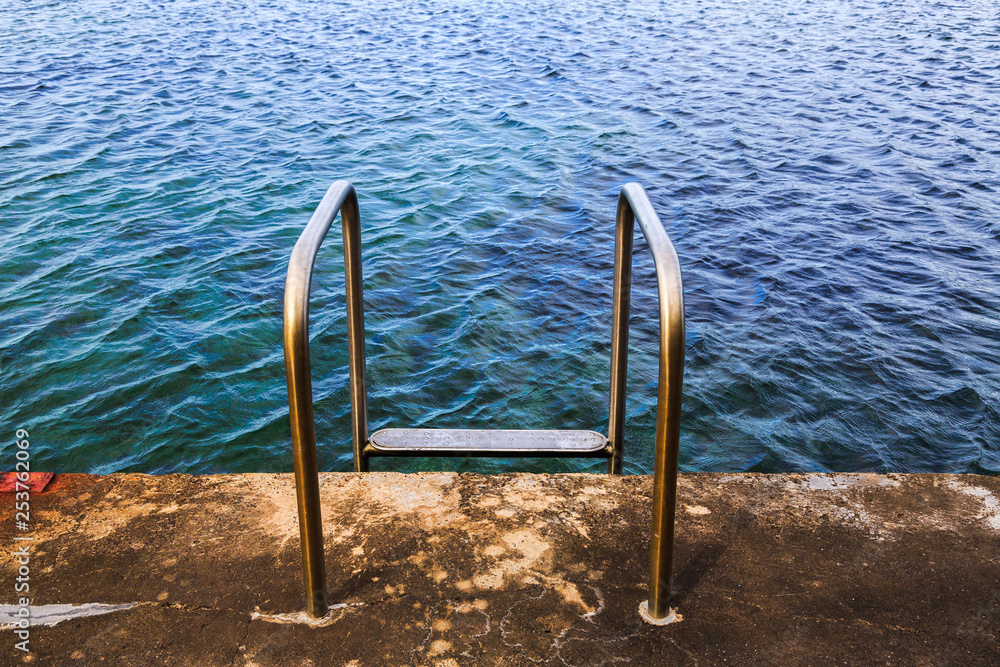 A chrome steel ladder leads into an ocean pool for recreational swimming, South Coast, New South Wales. Australia. A chrome steel ladder leads into an ocean pool for recreational swimming, South Coast, New South Wales. Australia.