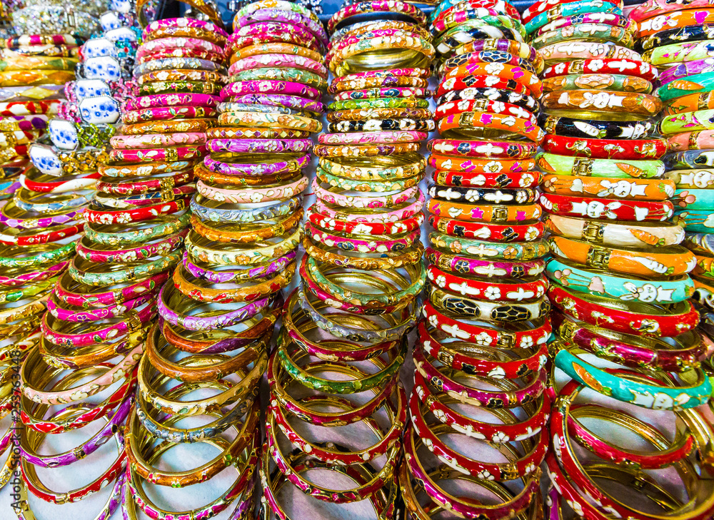A stack of multi colored shiny metal bracelets on a table in a tourist market place gift shop store.  Hong Kong.