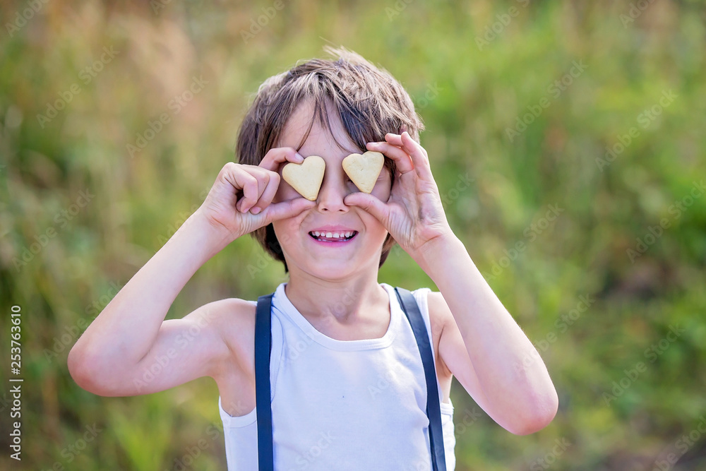 Sweet preschool child, boy, holding cookies in front of his eyes, smiling, nature background Sweet preschool child, boy, holding cookies in front of his eyes, smiling, nature background