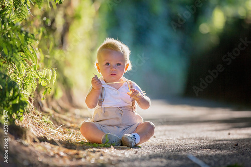Little baby boy, toddler child, playing with leaves on a sunny path in the forest