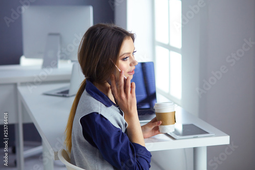 Focused attentive woman in headphones sits at desk with laptop, looks at screen, makes notes, learns foreign language in internet