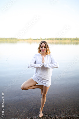 The girl is standing in a yoga pose on one leg by the river