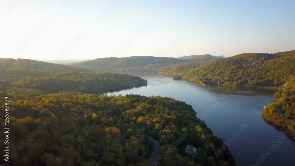 Smooth panning aerial / drone shot over the forest on a driveway, cottages and a lake during summer season with green, yellow and orange trees on the background. Smooth panning aerial / drone shot over the forest on a driveway, cottages and a lake during summer season with green, yellow and orange trees on the background.
