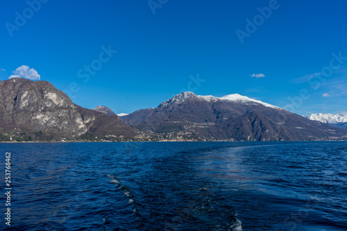 Italy, Bellagio, Lake Como, Cadenabbia, SCENIC VIEW OF SEA BY MOUNTAINS AGAINST BLUE SKY © SkandaRamana