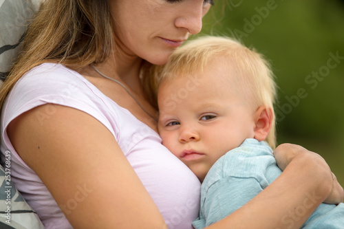 Young mother, holding her cute baby boy outdoor, cuddle him, kissing and huging, sitting outdoor on the porch
