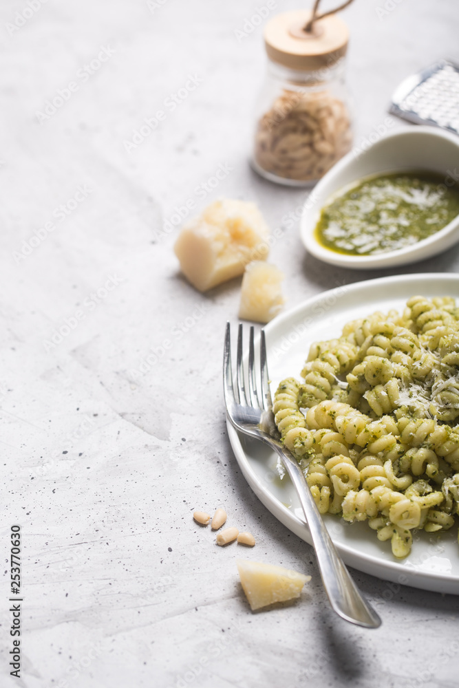 Plate of pasta fusilli with pesto sauce and parmesan cheese on gray concrete background Plate of pasta fusilli with pesto sauce and parmesan cheese on gray concrete background