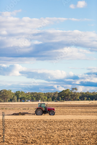 A farmer in a red tractor plowing land using a drag chain harrow.  Victoria  Australia.