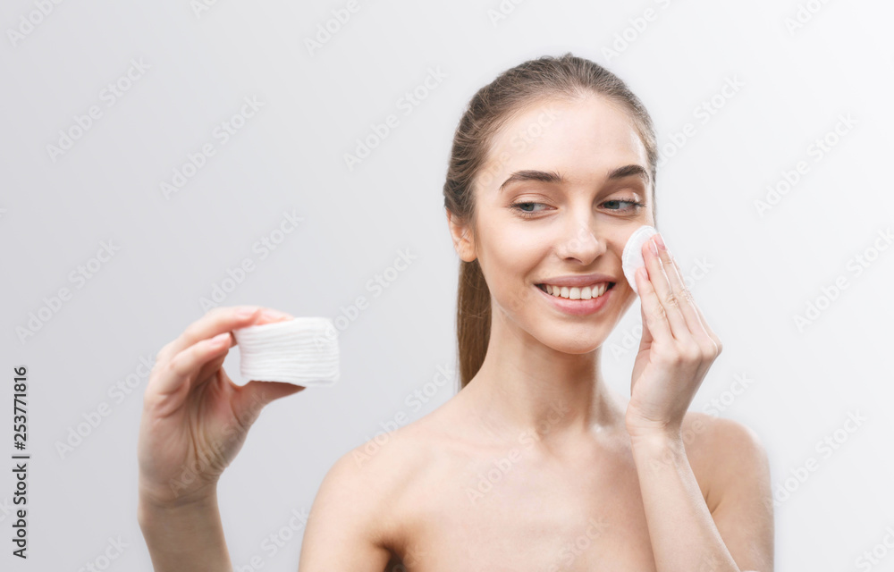 Woman holding cotton pads and looking on it while cleaning her face Woman holding cotton pads and looking on it while cleaning her face