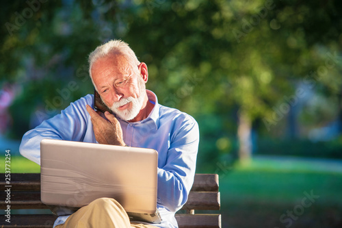 Business correspondence. Focused mature businessman using laptop while sitting in park photo