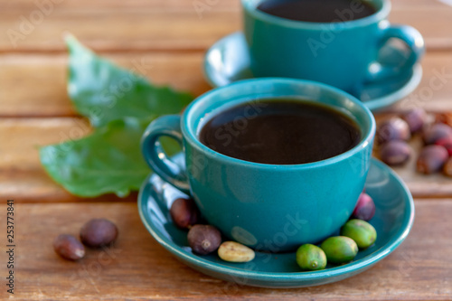 Cup with black coffee served outside with raw green  mature red and roasted coffee beans  decorated with green leaves from coffee plant