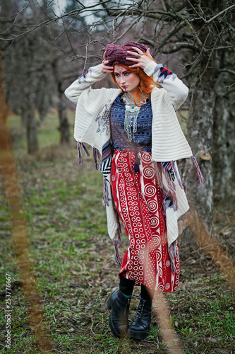 Extravagant redhead woman in ethnic national dress dancing or posing in a mistical forest