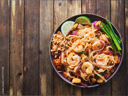 shrimp pad thai on plate in flat lay composition with copy space atop rustic wooden table