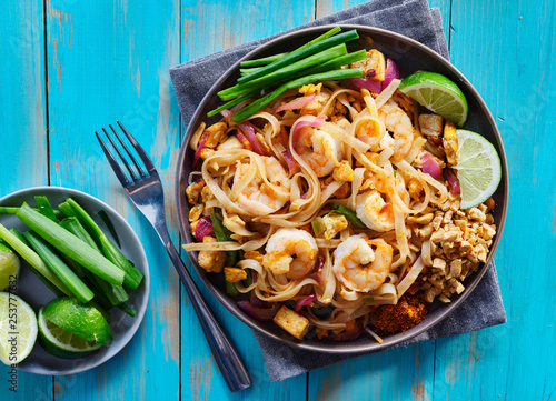 shrimp pad thai on plate in flat lay composition with copy space atop of colorful wooden table