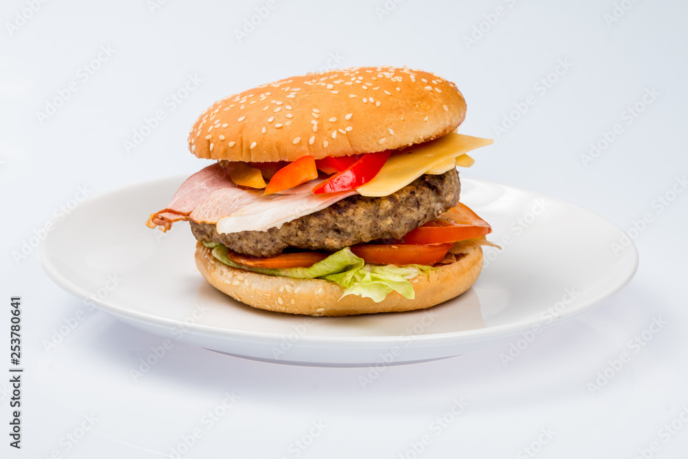cheeseburger with beef cutlet, bacon, tomatoes and cheese slices, seasoned with sauce and green salad for a restaurant menu on a white isolated background cheeseburger with beef cutlet, bacon, tomatoes and cheese slices, seasoned with sauce and green salad for a restaurant menu on a white isolated background