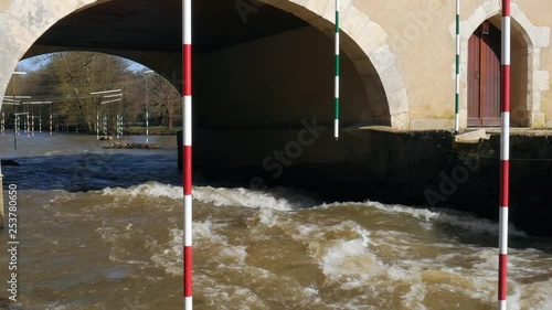 A bumpy river under the bridge with hanging striped gates for kayakers to practice slalom. photo