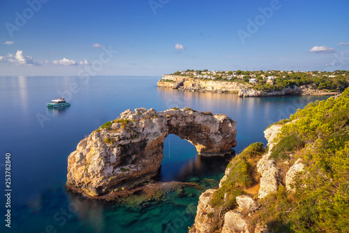Es Pontas in Mallorca, natural arch in the Mediterranean sea at sunrise with a boat anchored nearby and holiday villas and apartments in the background. Rope for extreme climbing hanging photo