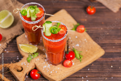 Two glasses of tomato juice decorated with fresh tomatoes  cucumber and leaves on a wooden background