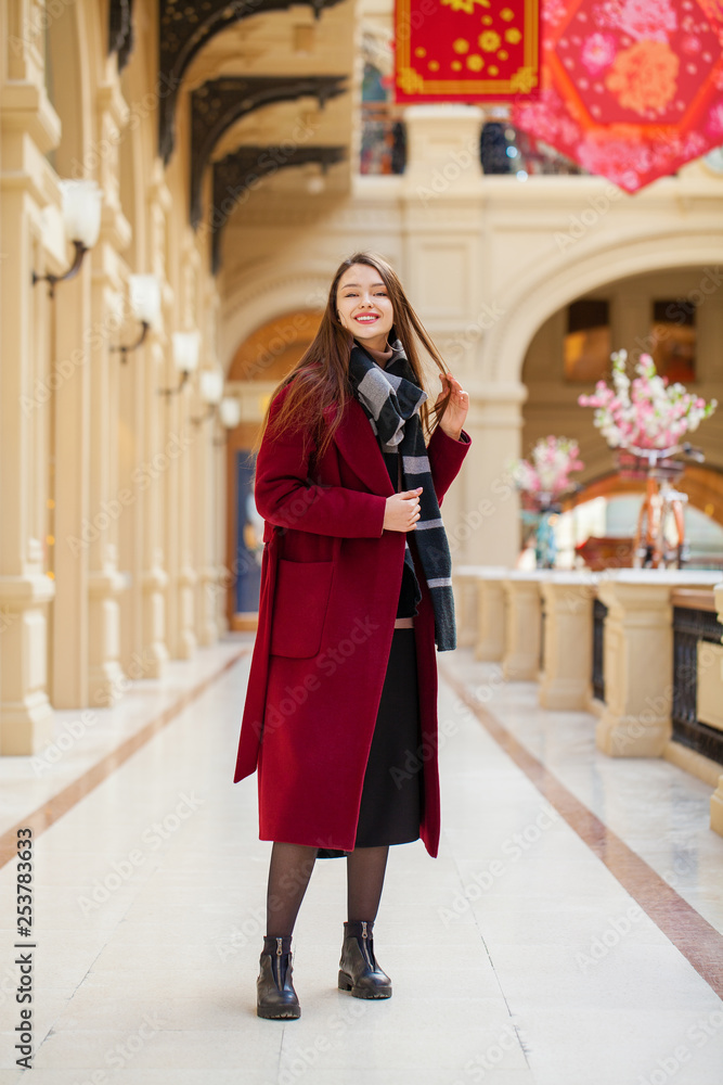 Fototapeta premium Beautiful girl in stylish in a long burgundy coat, indoor shop