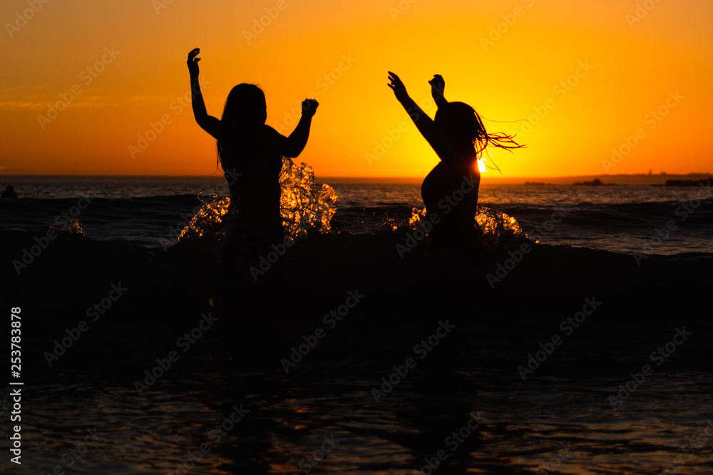 Girls jump with wave at sunset