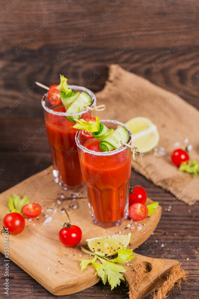 Two glasses of tomato juice decorated with fresh tomatoes, cucumber and leaves on a wooden background Two glasses of tomato juice decorated with fresh tomatoes, cucumber and leaves on a wooden background