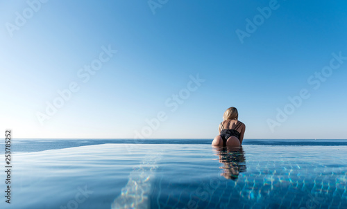 concept of vacation by the sea in the pool. girl in a luxurious swimsuit on the edge of a panoramic pool against the sea