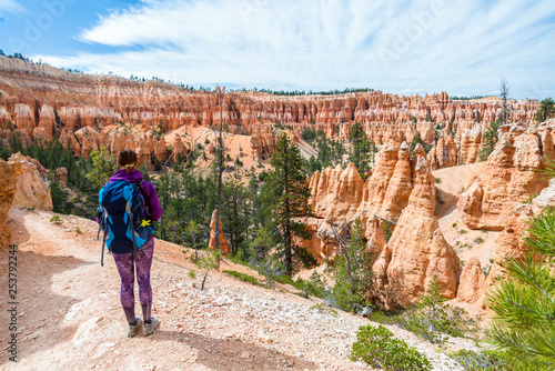 Hiker woman in Bryce Canyon taking a photo, looking and enjoying view during her hike wearing hikers backpack. Bryce Canyon National Park landscape, Utah, United States.