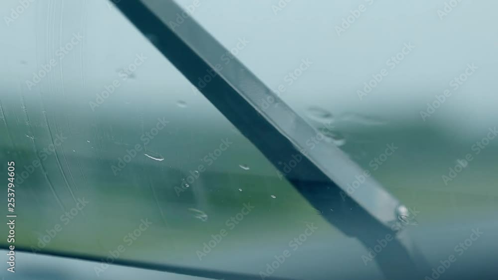 close view from car cabin black metal wiper works under light rain against green blurry silhouette close view from car cabin black metal wiper works under light rain against green blurry silhouette